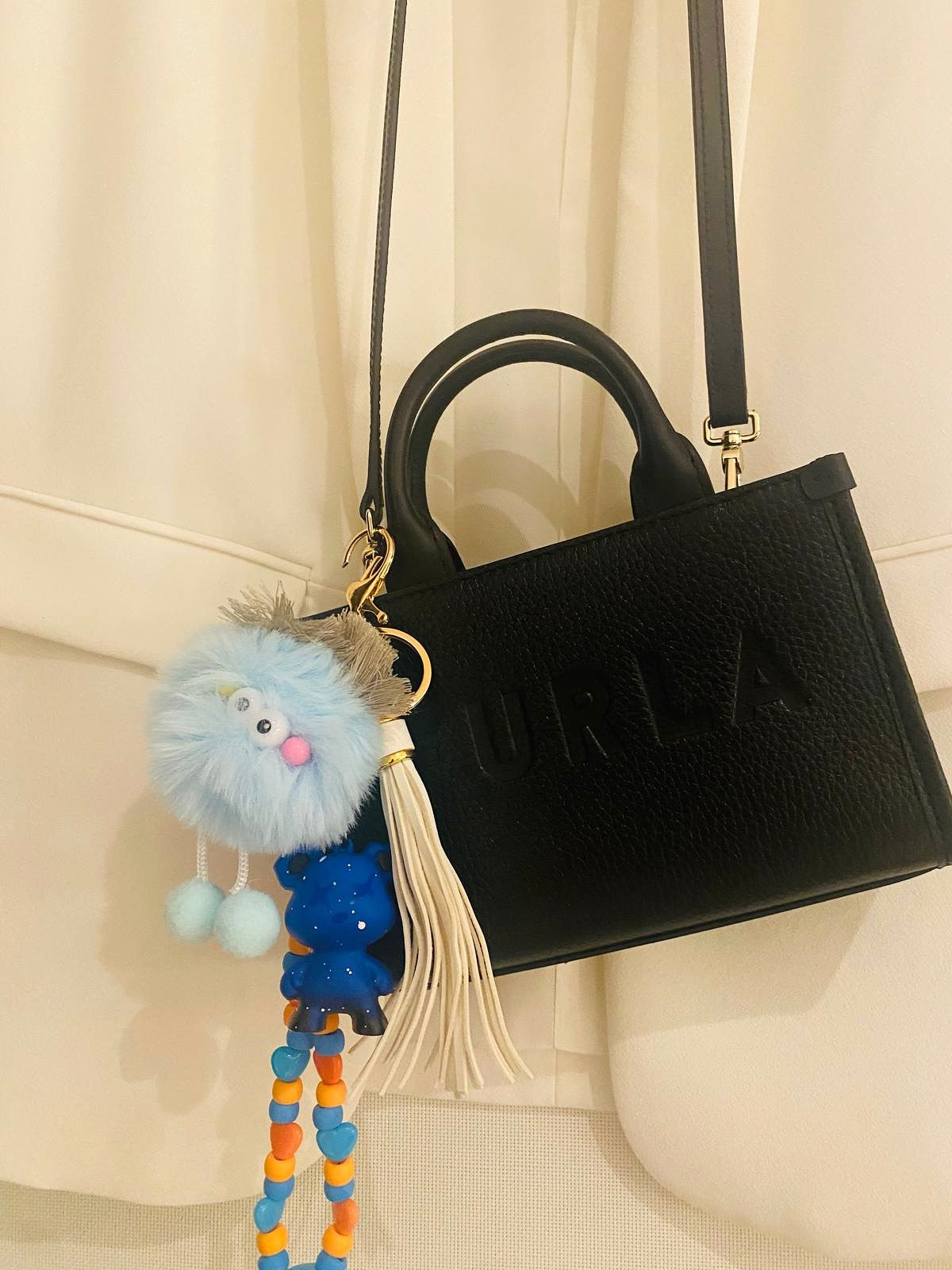 Black Furla bag, Soho Disco Bag with gold chain strap, featuring a pom-pom charm and beaded keychain charm.

