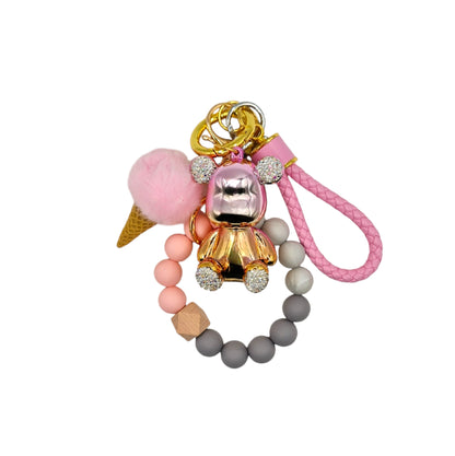 Cute and colorful ice cream-themed keychain featuring a pink pom-pom, a gold metallic teddy bear charm with diamond ears, and a beaded pink leather like strap.