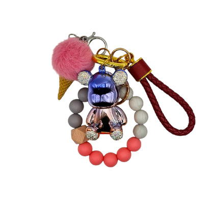 Cute and colorful ice cream-themed keychain featuring a pink pom-pom, a gold metallic teddy bear charm with diamond ears, and a beaded red leather like strap.