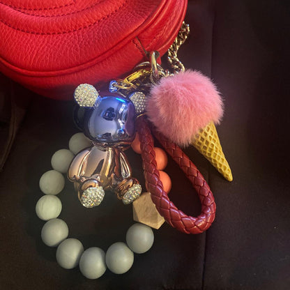 Cute and colorful ice cream-themed keychain featuring a pink pom-pom, a gold metallic teddy bear charm with diamond ears, and a beaded leather like strap.